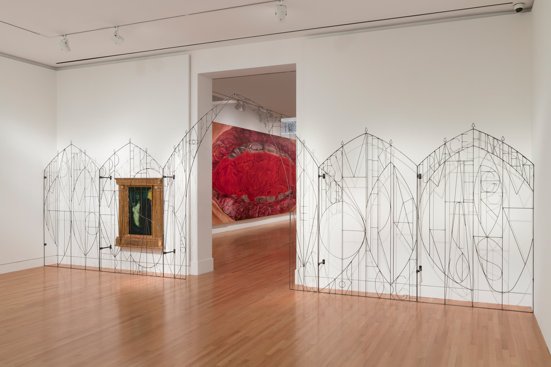 Image is a photo of a slim steel gate with letters across its form. Behind the gate on the wall is a painting of a woman, and a large doorway into another gallery revealing a glimpse of a paintings of a mouth.